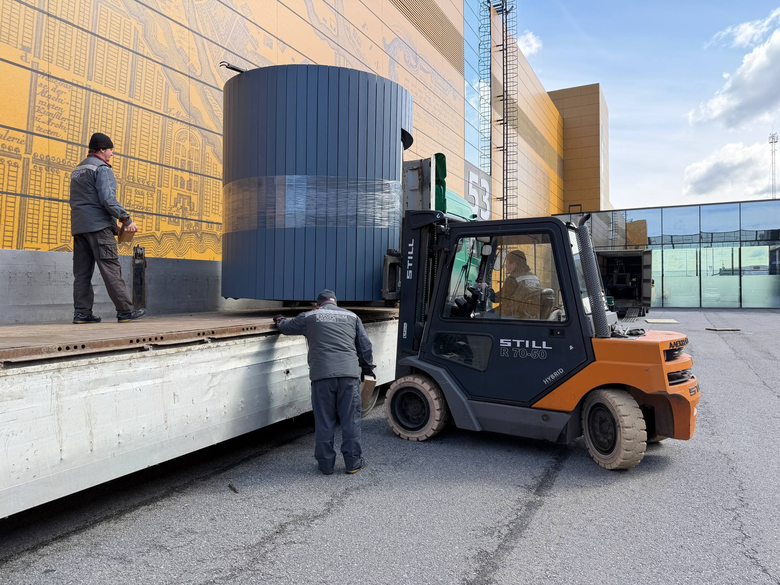 Gray cylindrical sauna being loaded onto a flatbed by forklift
